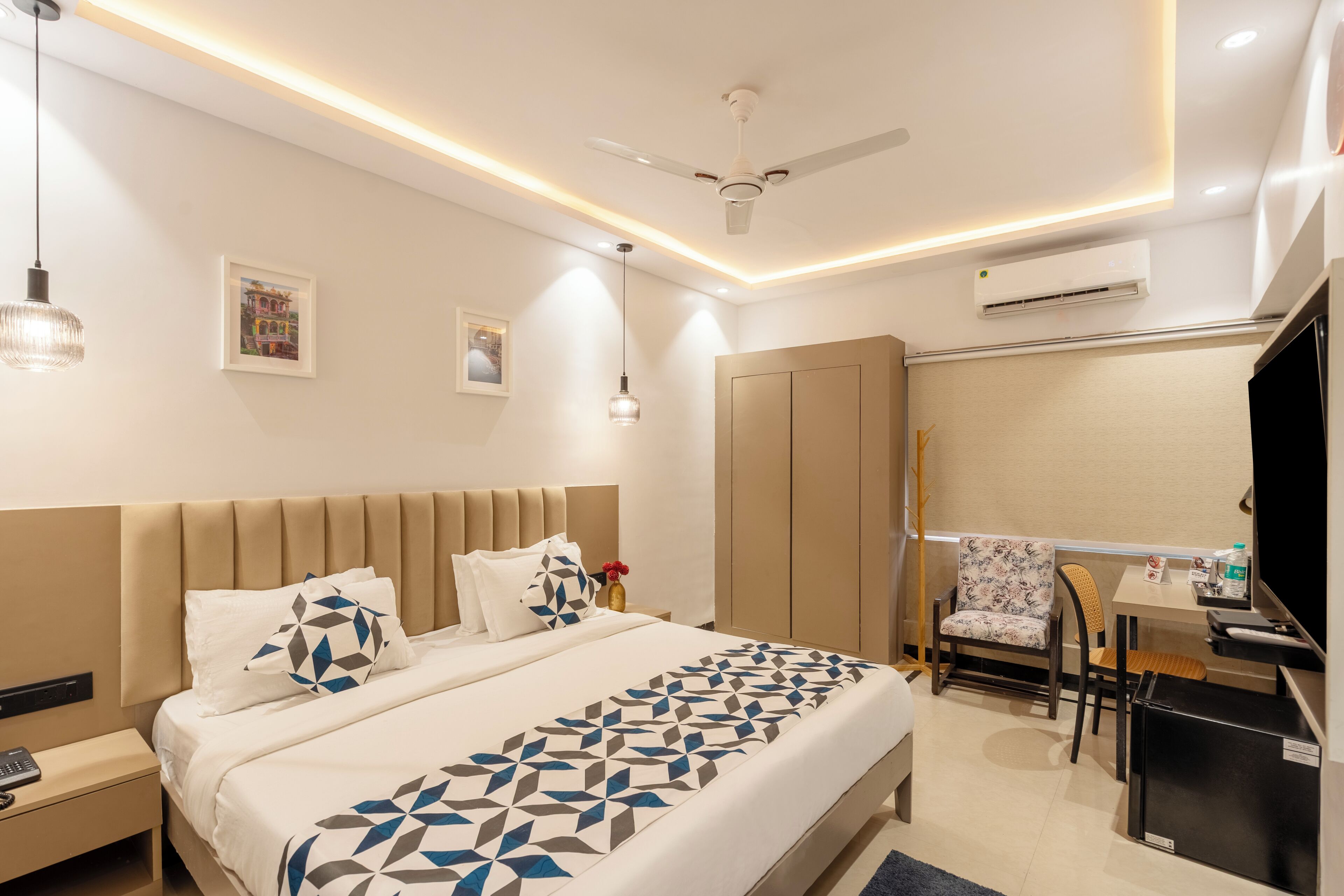 A modern hotel room with a large bed, a desk with a chair, a ceiling fan, and an air conditioning unit.