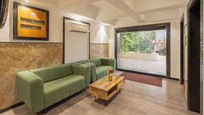 Un área de recepción con un sofá verde, una mesa de centro de madera y un amplio ventanal con vistas al exterior.