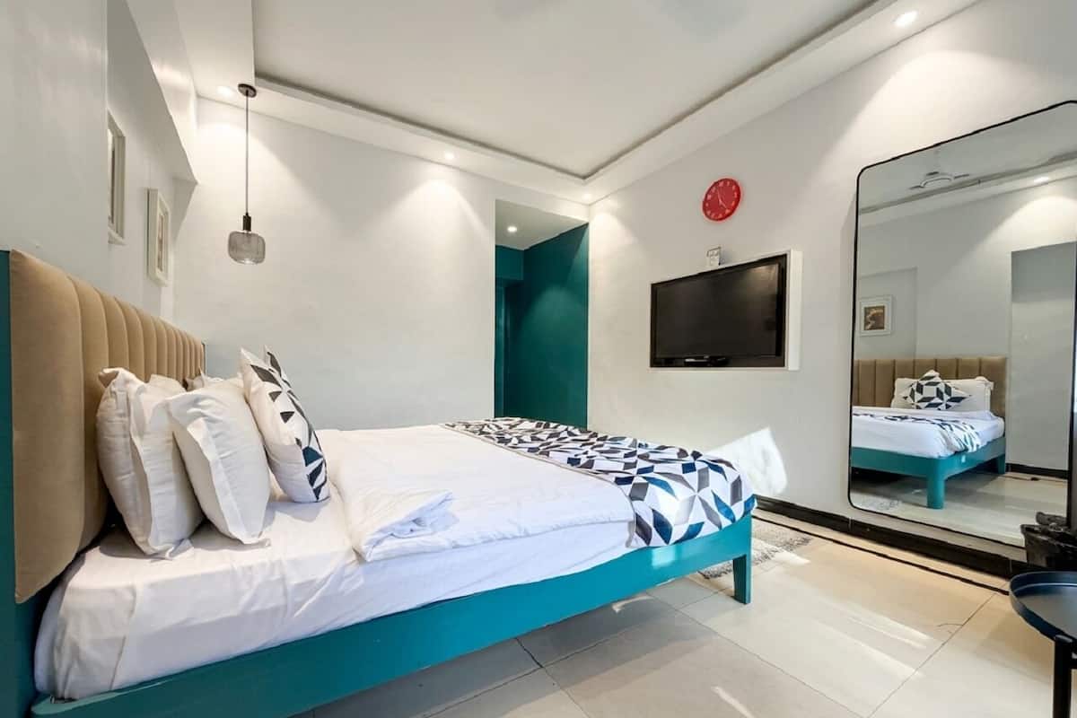 Moderni hotellihuone, jossa on sänky, televisio, peili ja seinällä oleva kello.