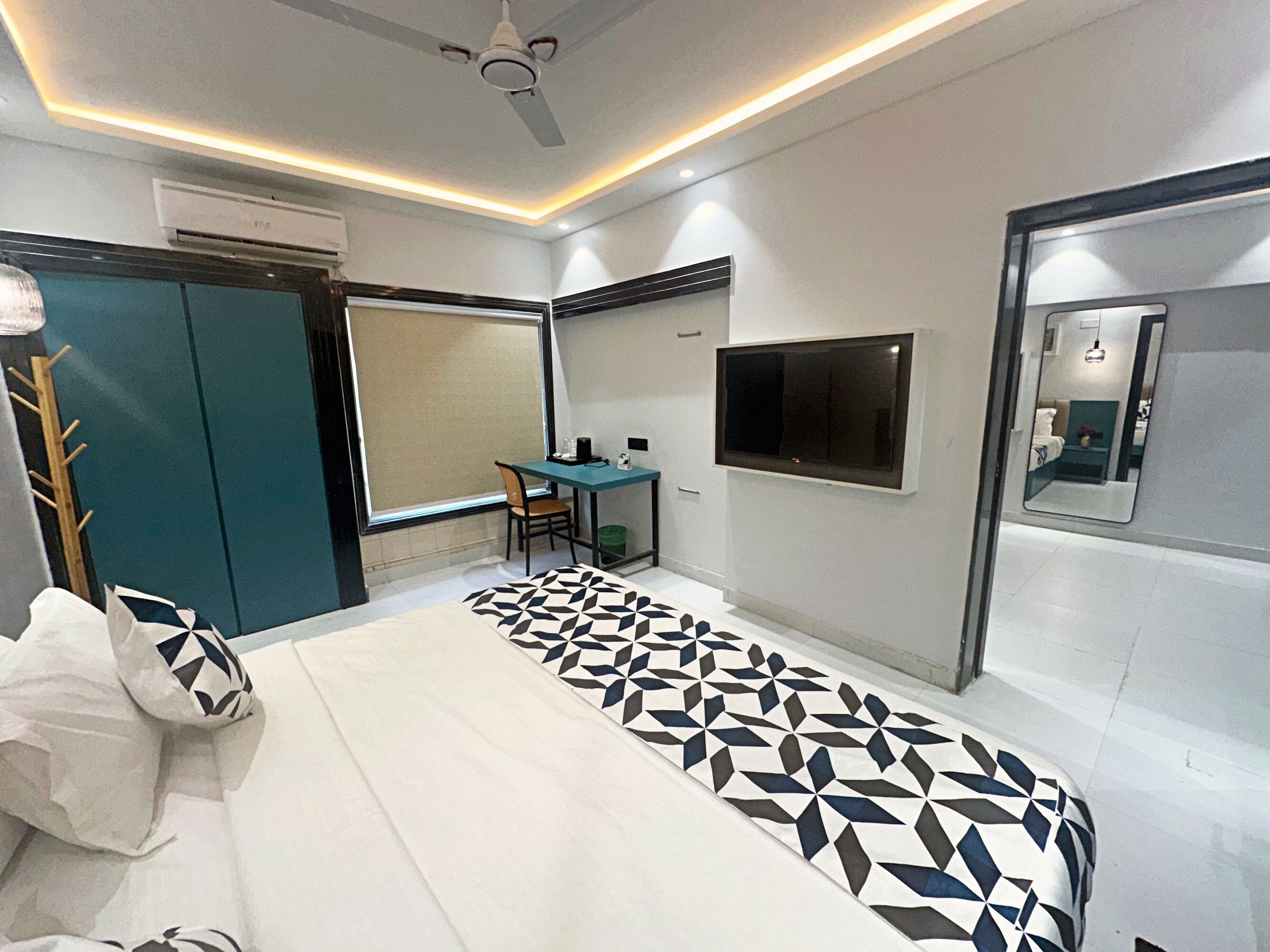 Un dormitorio moderno con cama, escritorio, silla, televisor y armario.