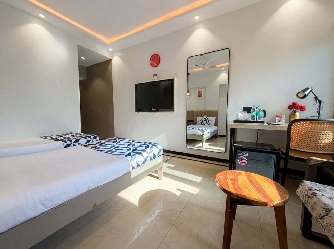 Une chambre d’hôtel équipée d’un lit, d’un bureau, d’une chaise, d’un petit réfrigérateur, d’une télévision et d’un miroir.