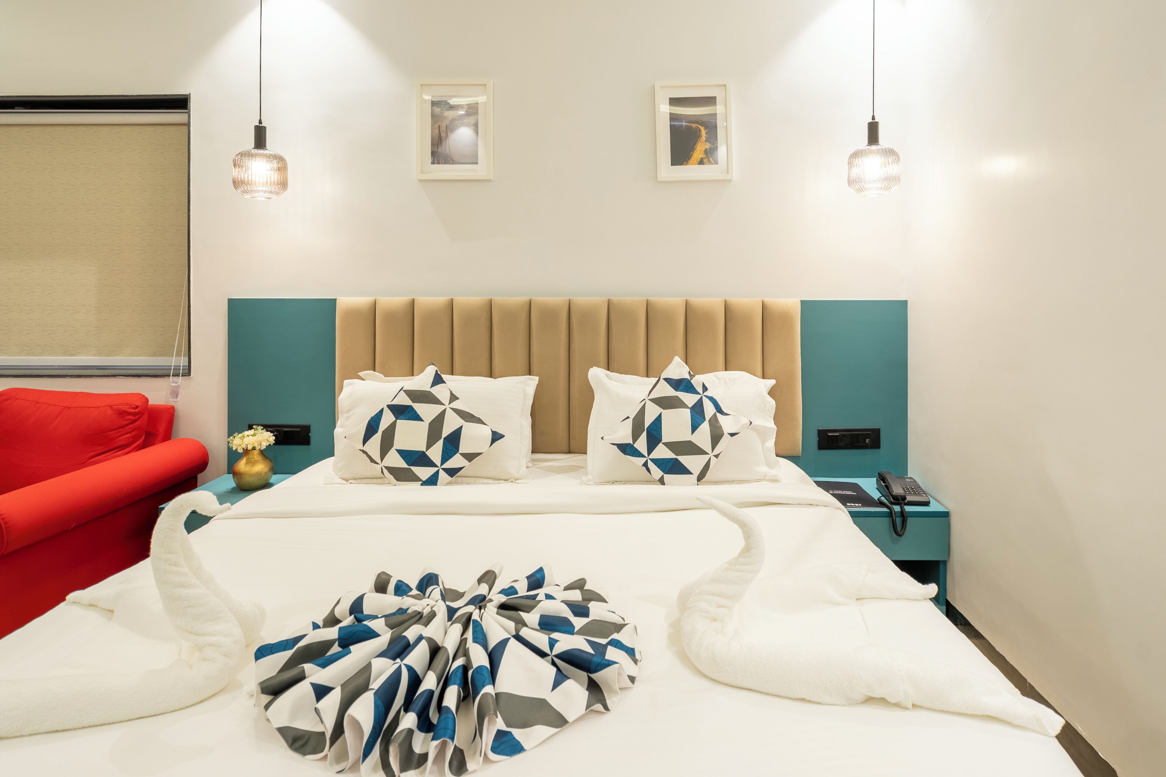 A hotel room with a bed, a red chair, a nightstand with a phone, and two wall-mounted lights.