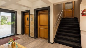 A hotel lobby with a wooden reception desk, a black staircase, and a fire extinguisher on the wall. - asar Elite by Orion Hotels (Mumbai)