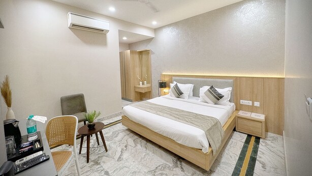 Una habitación de hotel moderna con una cama grande, un escritorio con computadora, una silla y una pequeña mesa con una planta.