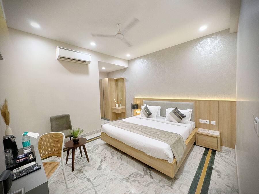 Quarto de hotel moderno com uma cama grande, uma escrivaninha com computador, uma cadeira e uma pequena mesa com uma planta.