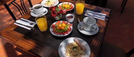 A breakfast table with plates of food, a cup of coffee, a glass of orange juice, and a small vase with flowers.