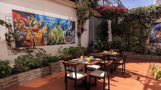 Un espace extérieur aménagé pour les repas, avec une fresque murale, un sol en terre cuite et diverses plantes.