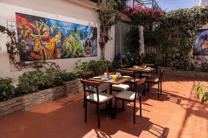 An outdoor dining area with a mural on the wall, terracotta flooring, and various plants. - KUSKA MARISCAL (Cusco)