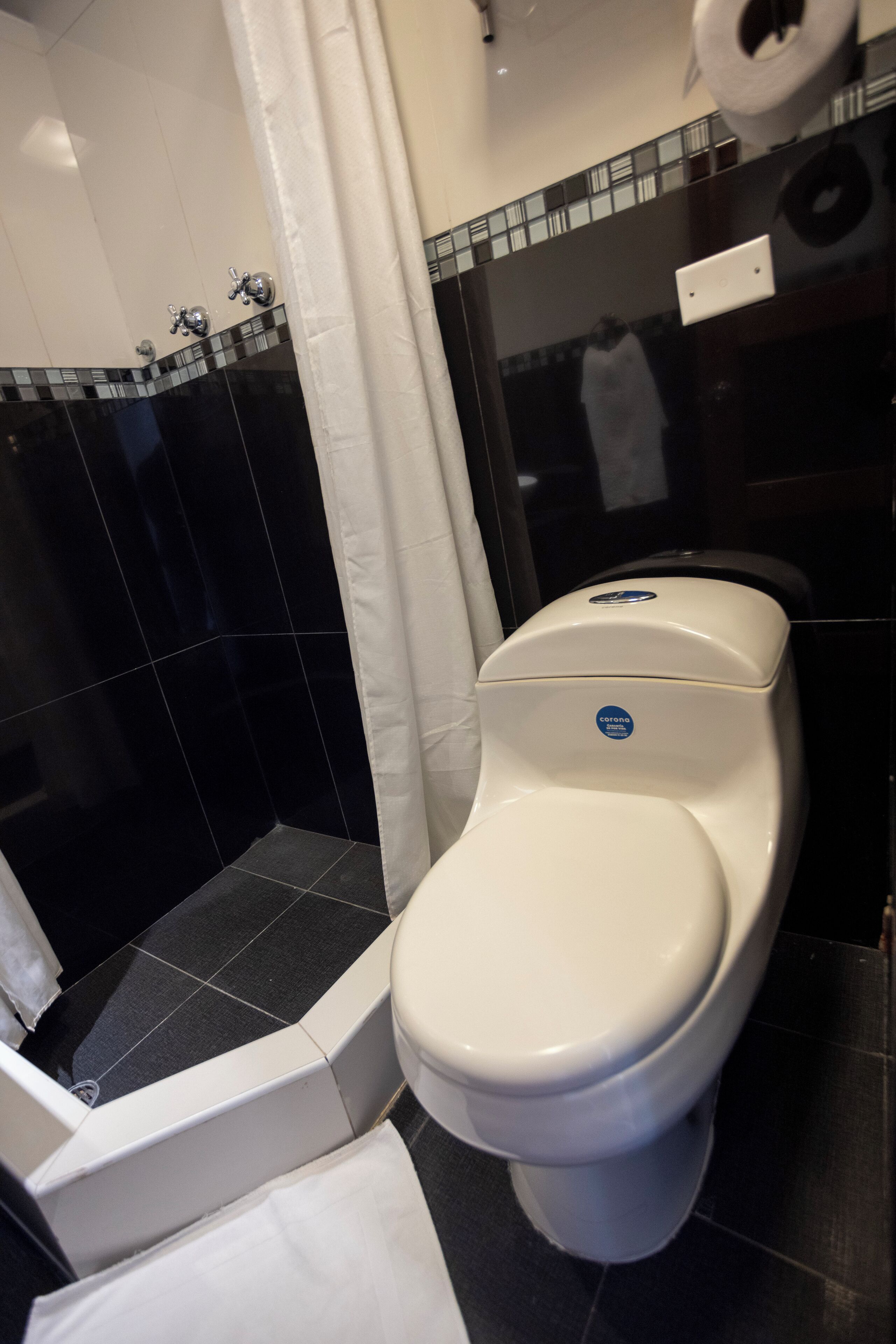 Ein Badezimmer mit Toilette, einer Duschkabine mit schwarzen Fliesen und einem weißen Vorhang.