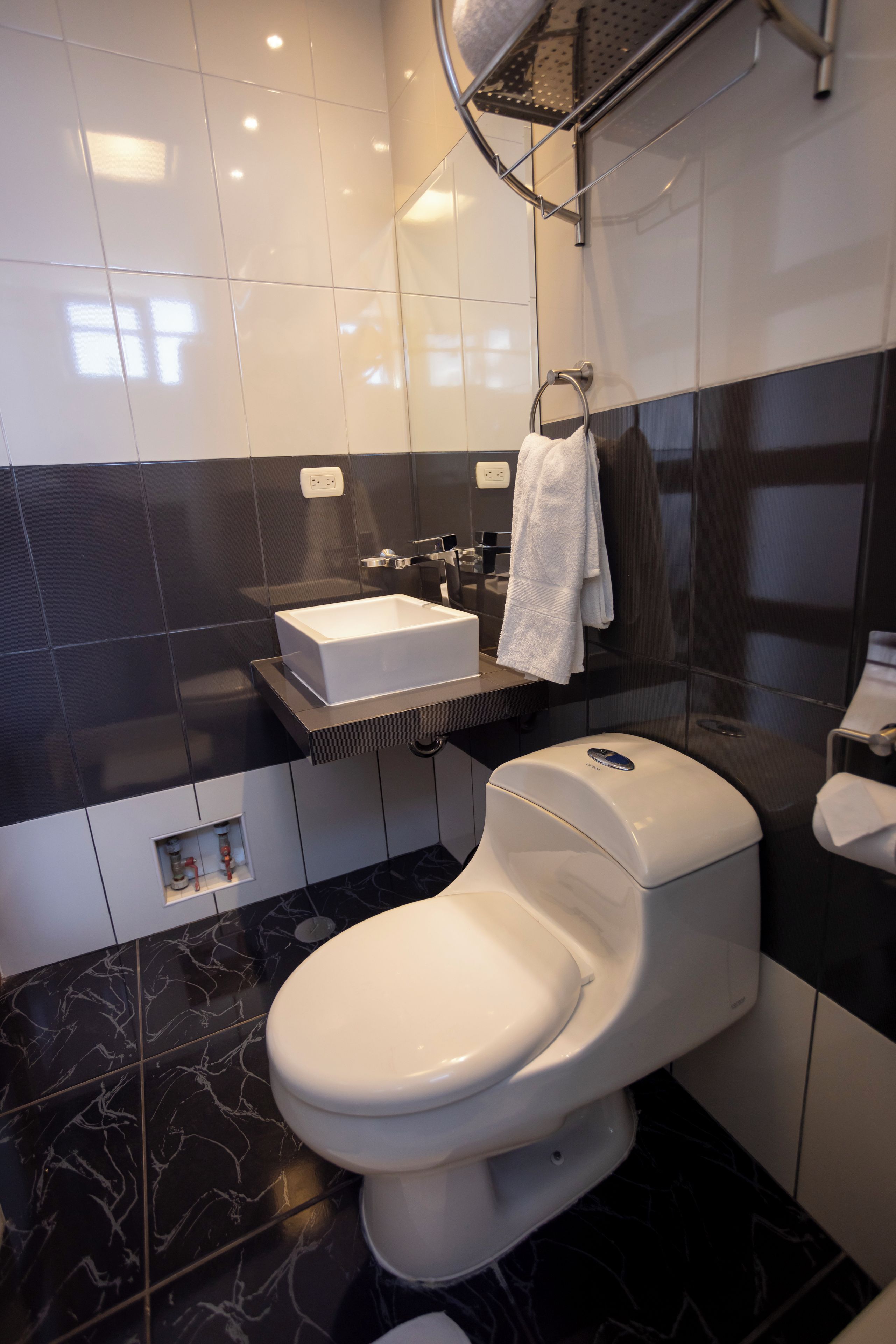 Un baño moderno con inodoro blanco, tocador con espejo y salpicadero de azulejos negros.