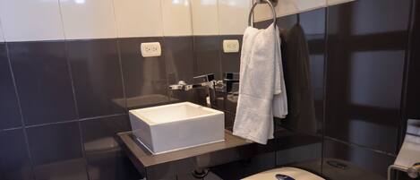 Un baño moderno con inodoro blanco, tocador con espejo y salpicadero de azulejos negros.