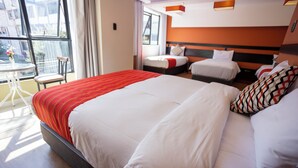 Une chambre d’hôtel avec un grand lit, un lit plus petit, une chaise et une table près d’une fenêtre.