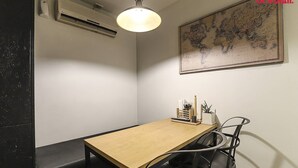 Una habitación con una mesa de madera, sillas negras, un mapa en la pared y una lámpara en el techo.