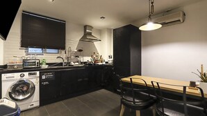 Una cocina moderna con lavadora, zona de comedor con mesa y sillas, y un armario negro.