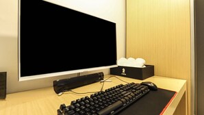Una habitación de hotel moderna con una televisión de pantalla plana grande, un teclado negro y un ratón sobre un escritorio de madera.