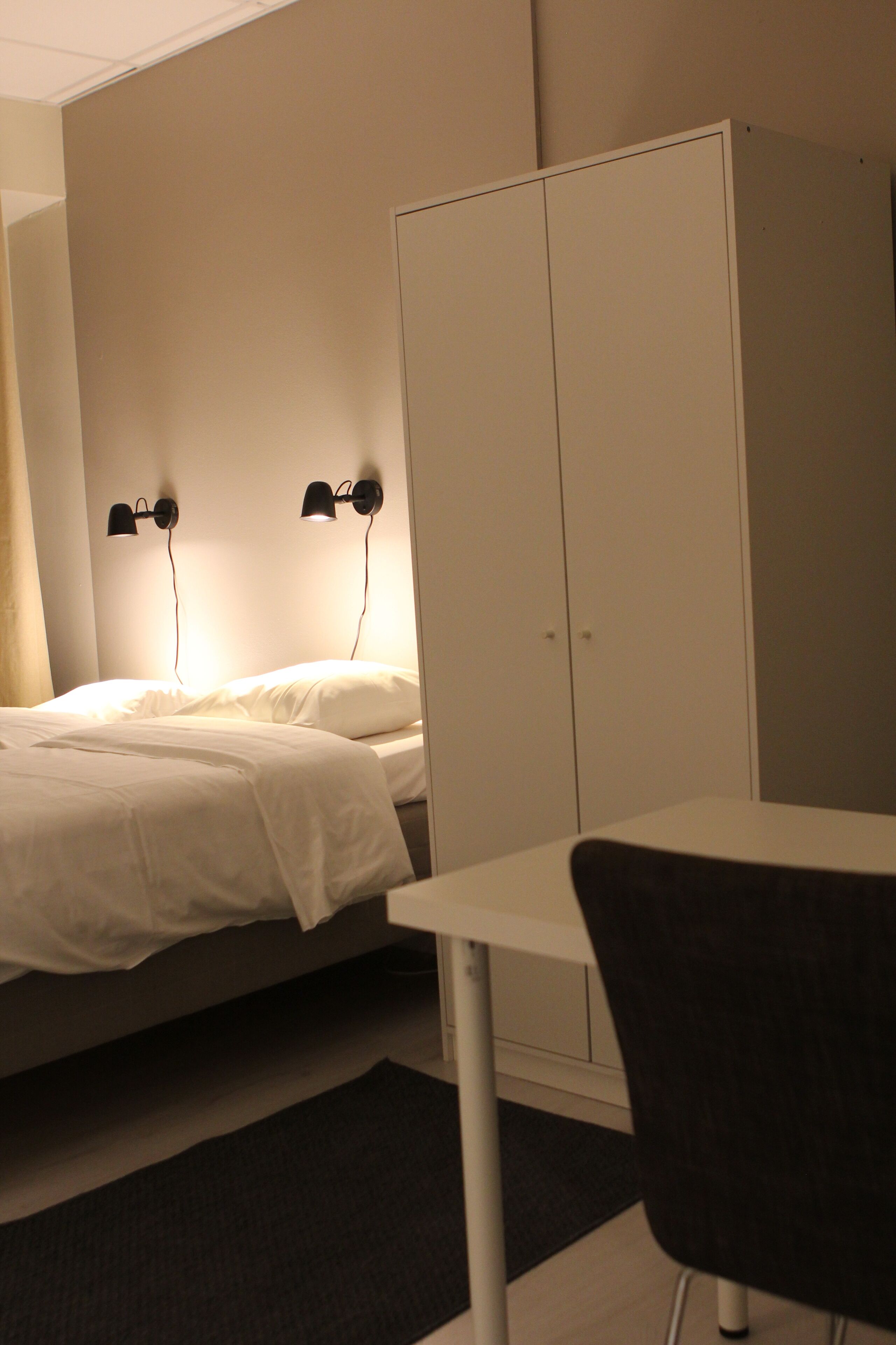 Ein Schlafzimmer mit einem Bett, Nachttischlampen, einem Kleiderschrank und einem Tisch mit Stuhl.