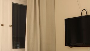 Habitación de hotel con cama, escritorio, dos sillas, televisor y ventana con cortinas.