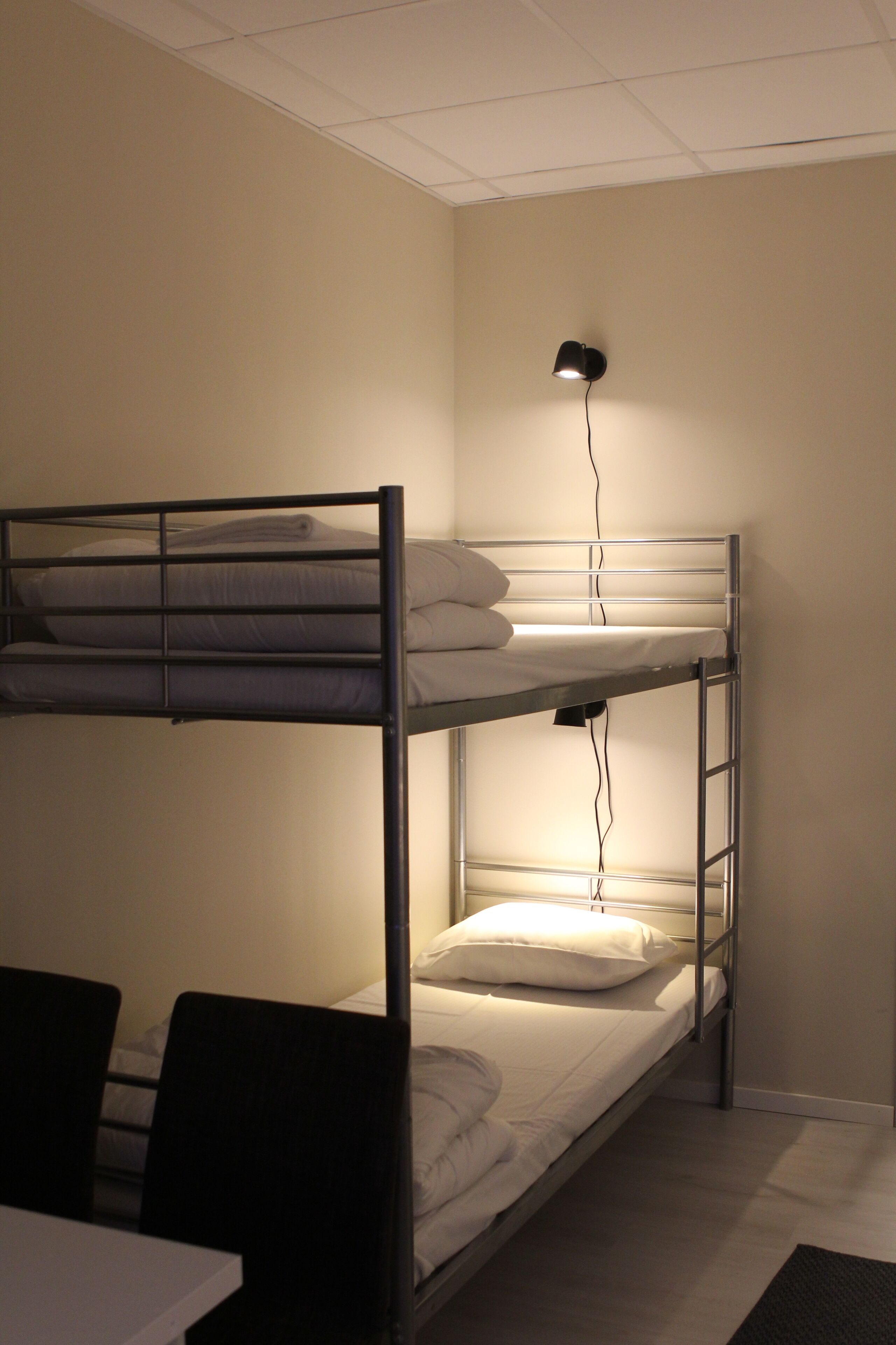 Une chambre avec un lit superposé, un bureau et des chaises, une lampe fixée au mur et un plafond orné d’un motif en réseau.