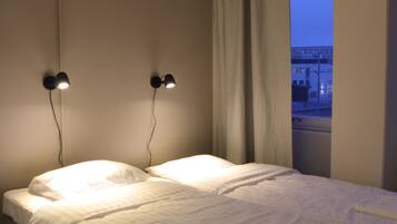 Habitación de hotel con una cama, dos lámparas fijadas a la pared y una ventana con cortinas.