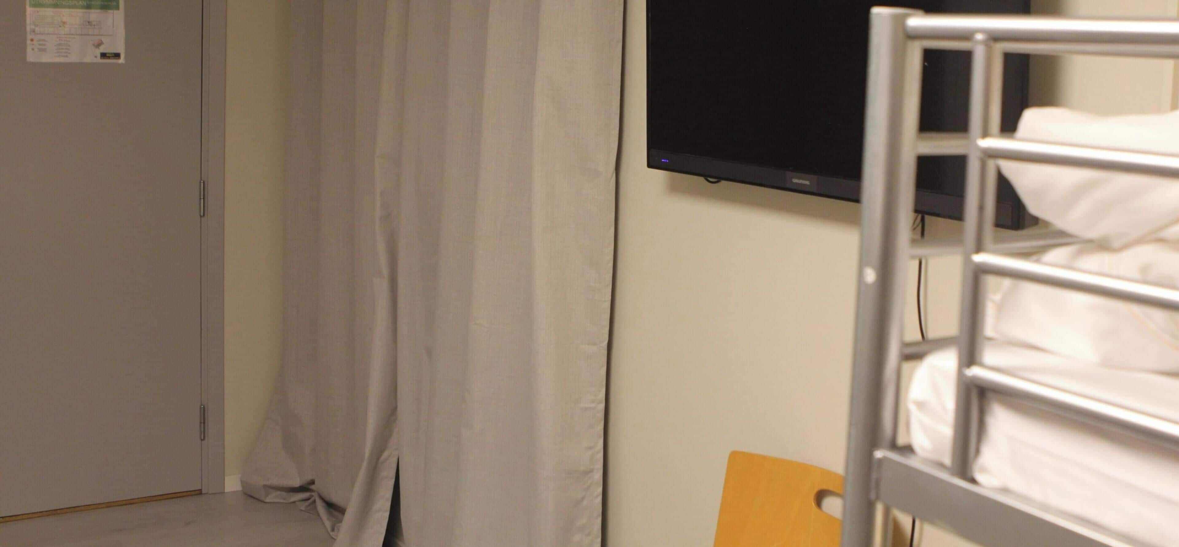 Ein 4-Bett-Zimmer mit Gemeinschaftsbad, ohne Fenster und einem Fernseher an der Wand.