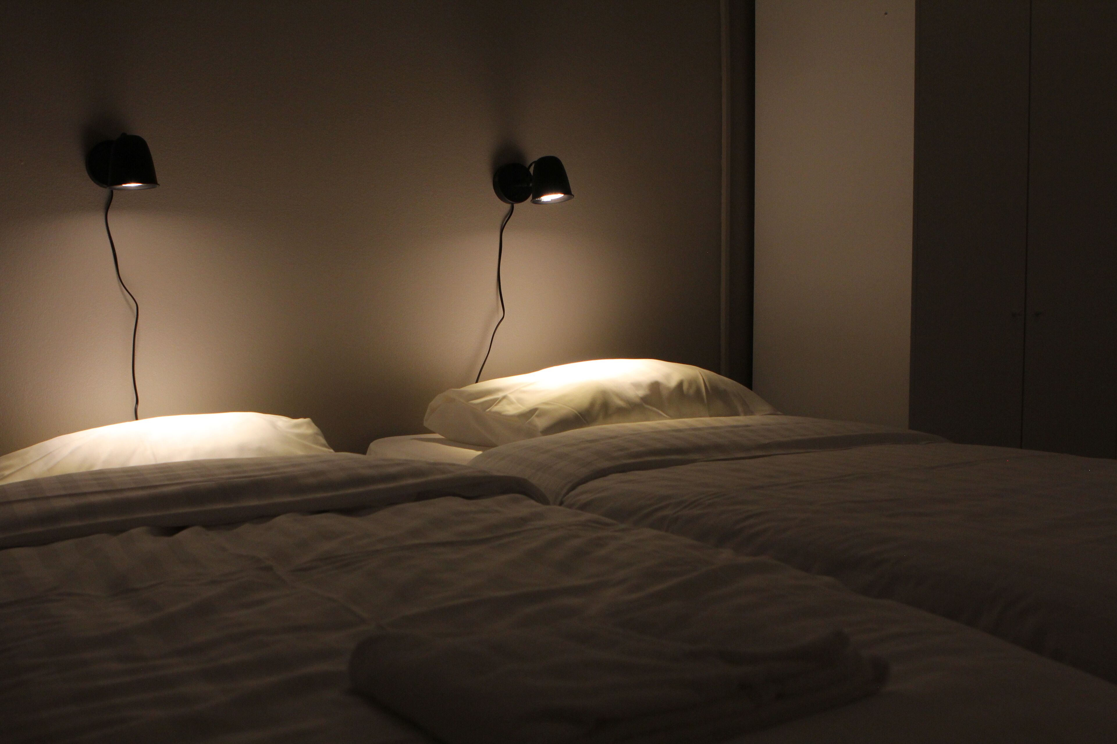 Une chambre avec deux lits, chacun étant muni d’une lampe fixée au mur.