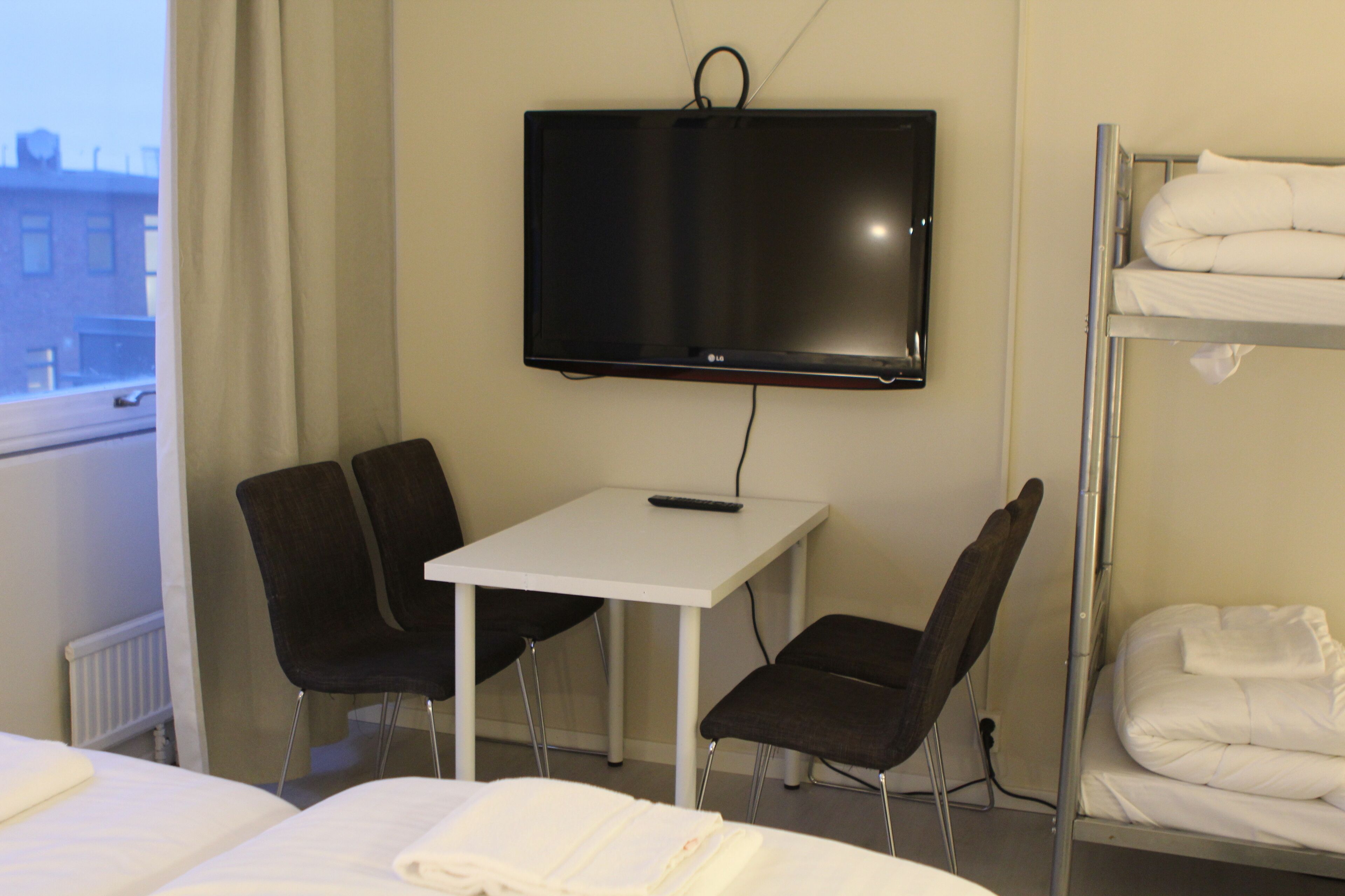 A hotel room with a bed, a desk with a chair, a TV mounted on the wall, and a bunk bed.