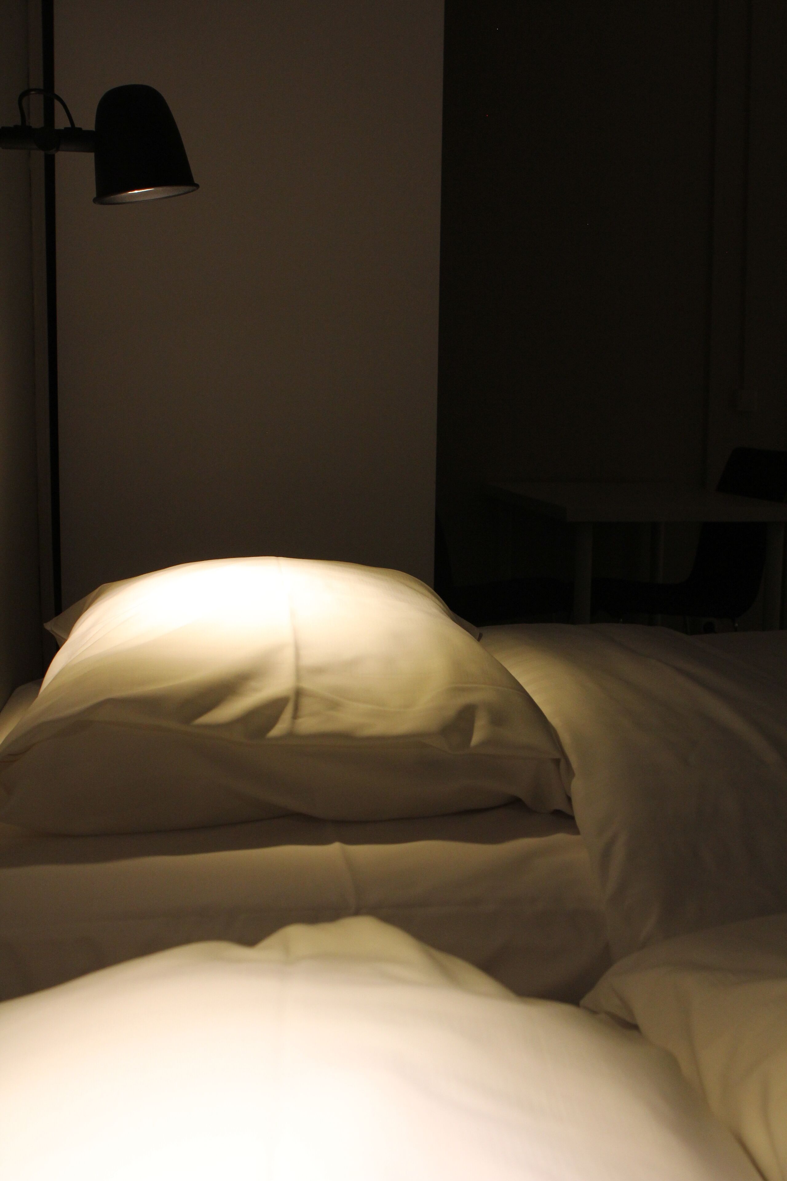 Hämärästi valaistu hotellihuone, jossa on sänky, lamppu ja tuoli.