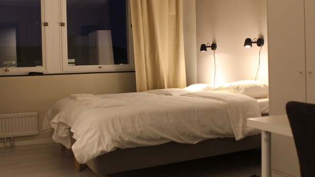 Un dormitorio con cama, ventana con cortinas, radiador y escritorio con silla.