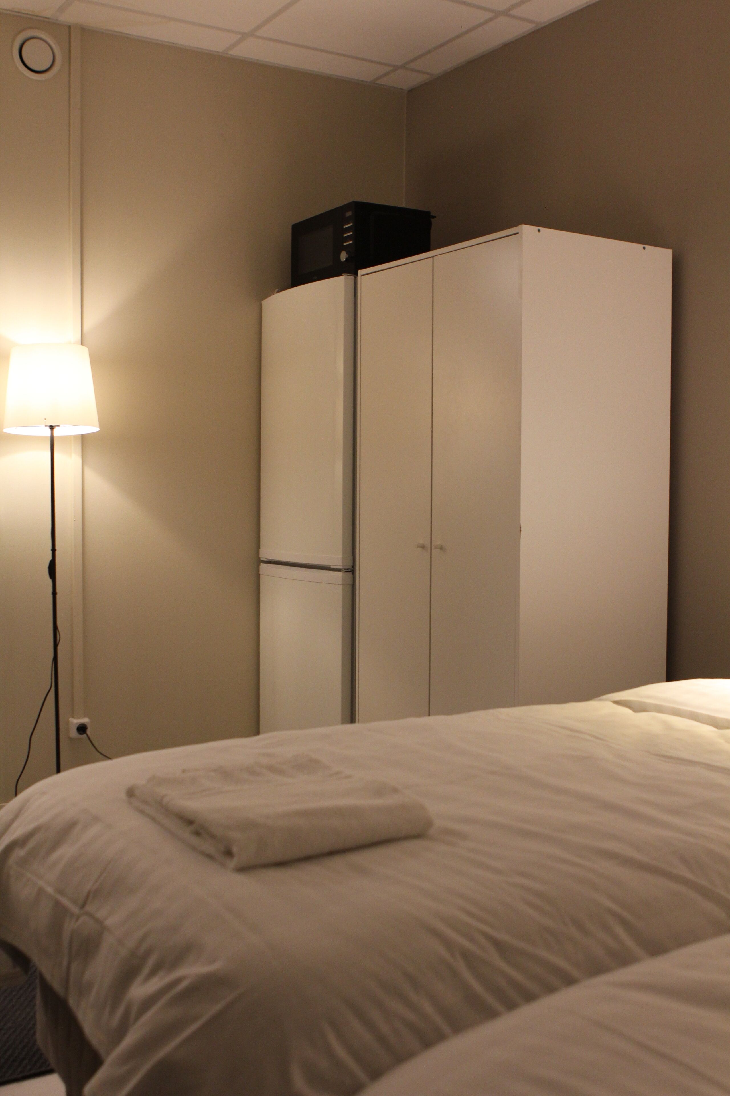 A hotel room with a bed, a wardrobe, and a floor lamp.