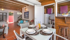 Comedor con una mesa dispuesta para cuatro personas, rodeado de paredes de madera y una cocina visible a través de un umbral abierto.