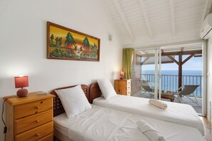 Una habitación de hotel con cama, mesita de noche, lámpara, un cuadro y un balcón con sillas y una mesa.