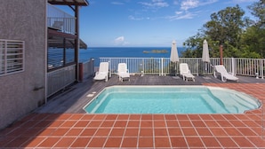 Zona de piscina con vista al océano, sillas de descanso blancas y una terraza amurallada.