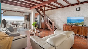 Amplia sala de estar con un televisor grande, una escalera de madera y un balcón con vistas.