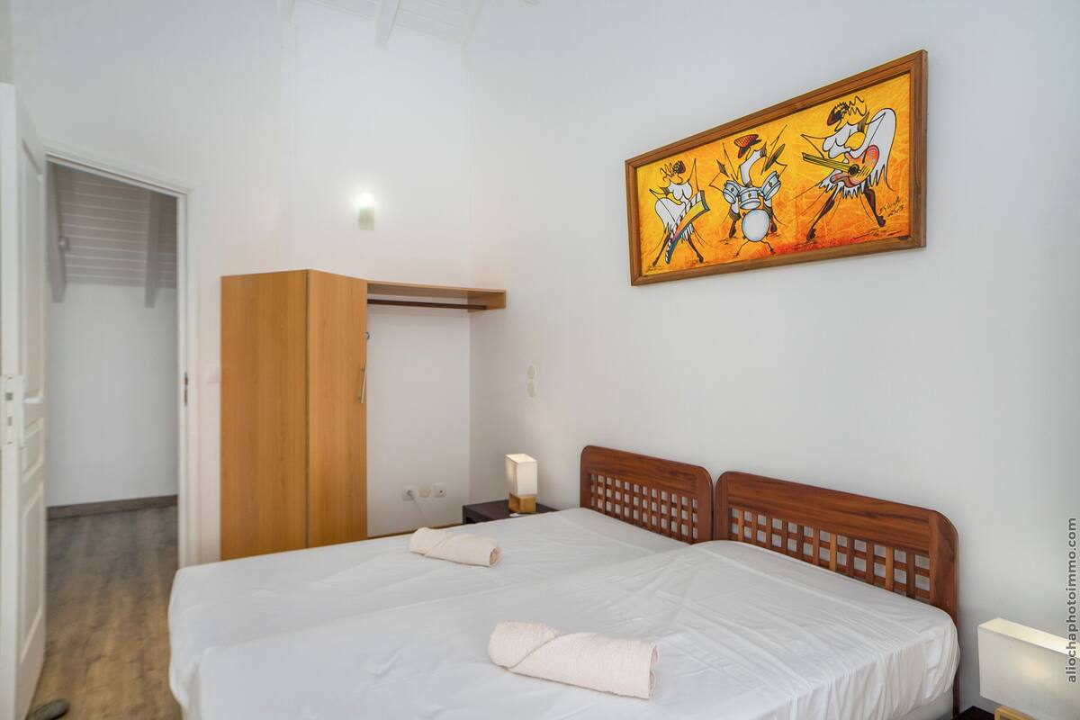 Una habitación de hotel con una cama grande, un armario de madera, un cuadro en la pared y una mesita de noche con una lámpara.