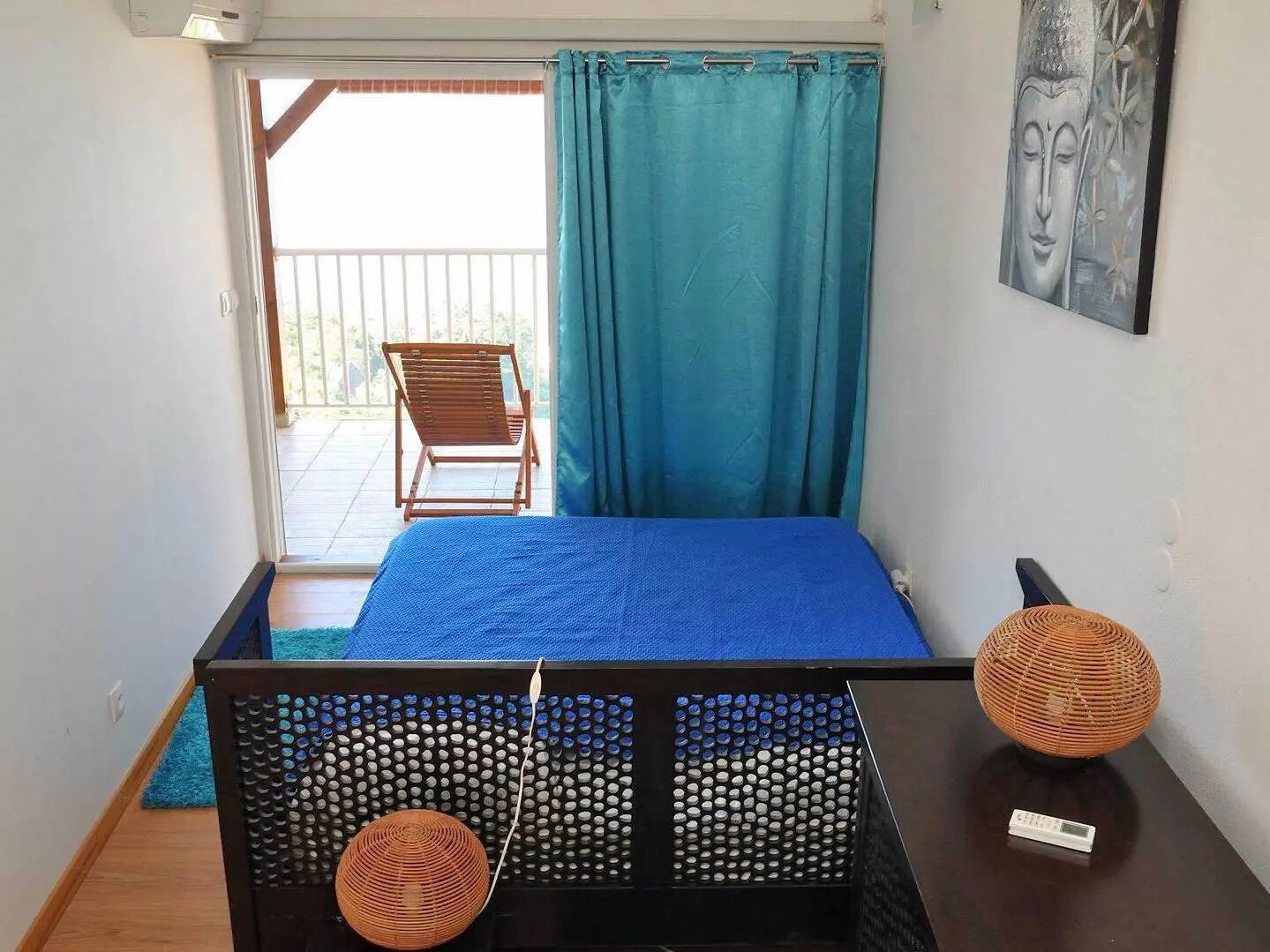 Ein Schlafzimmer mit Bett, Stuhl, einem Fenster mit Vorhängen und einem an der Wand befestigten Kunstwerk.