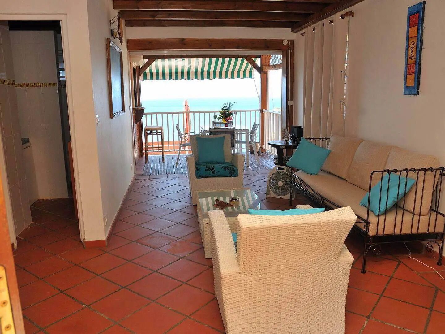 A spacious living area with a view of the sea, a balcony with a striped awning, and a dining area with chairs and a table.