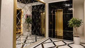A luxurious hallway with a black and white marble floor, a large mirror with a gold frame, and a chandelier. - HUMO PLAZA HOTEL (Fergana)