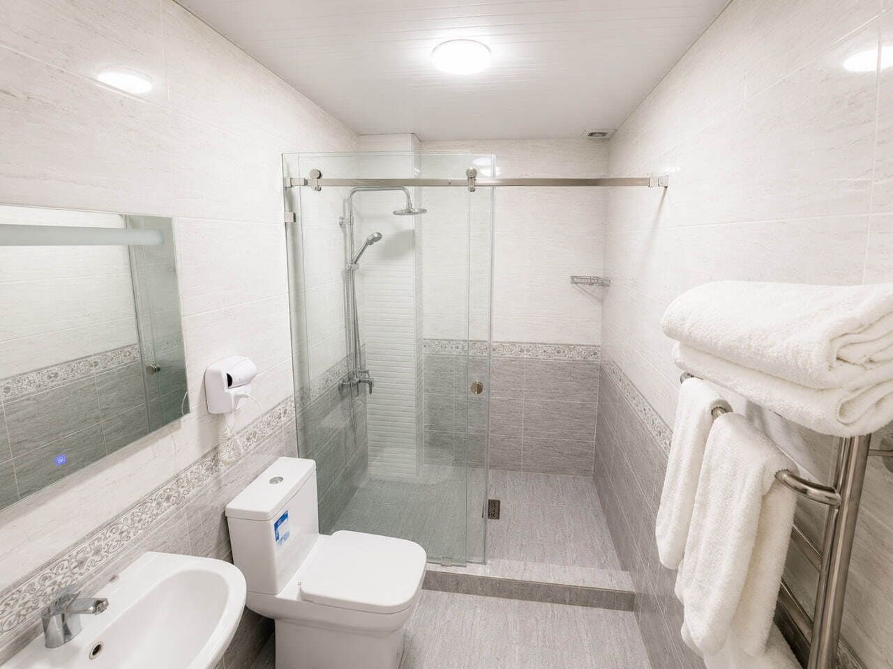 Uma casa de banho moderna com chuveiro envolto em vidro, sanita, lavatório e um porta-toalhas.