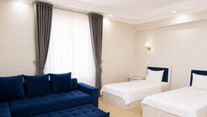 A hotel room with a blue sofa, two single beds, and a light-colored carpet. - HUMO PLAZA HOTEL (Fergana)