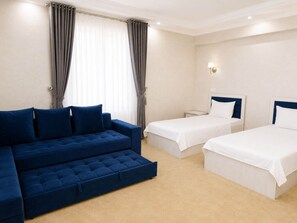 A hotel room with a blue sofa, two single beds, and a light-colored carpet. - HUMO PLAZA HOTEL (Fergana)