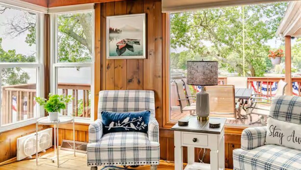 Una habitación acogedora con un sillón de cuadros, una mesita con lámpara y vistas al exterior a través de amplias ventanas.