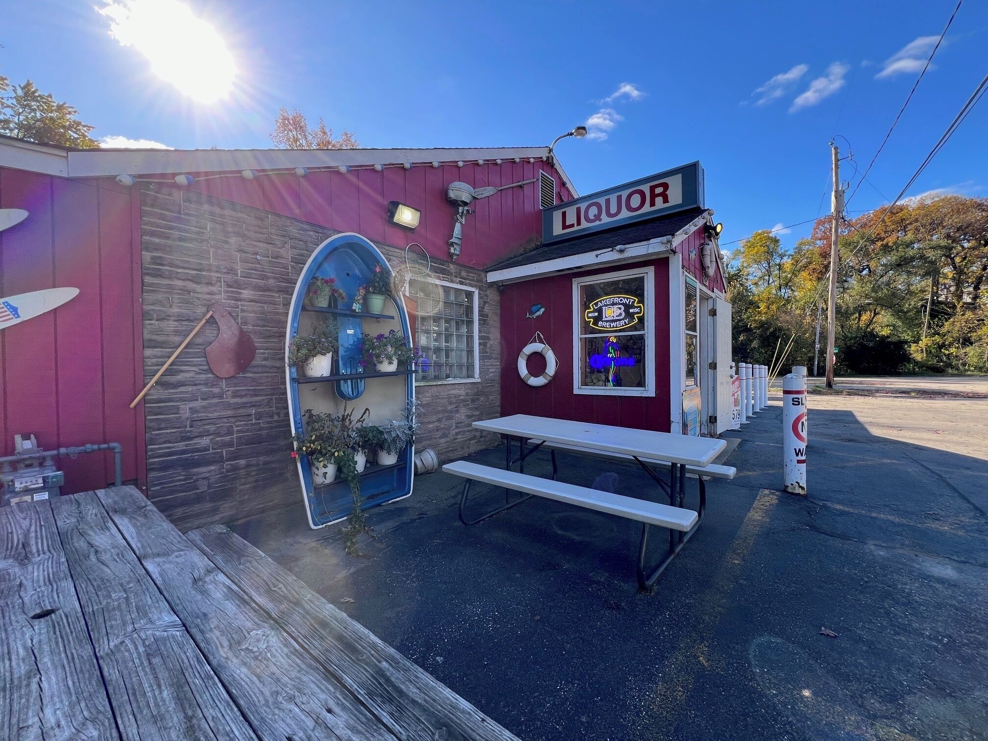 A small building with a 'LIQUOR' sign, a neon sign for 'LAKEFRONT BREWERY', and a wooden bench outside.