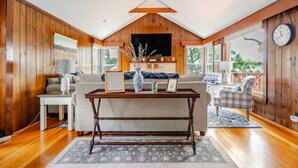 Un salón amplio con paredes de madera, un televisor grande y una zona de estar acogedora con un sofá y sillones.