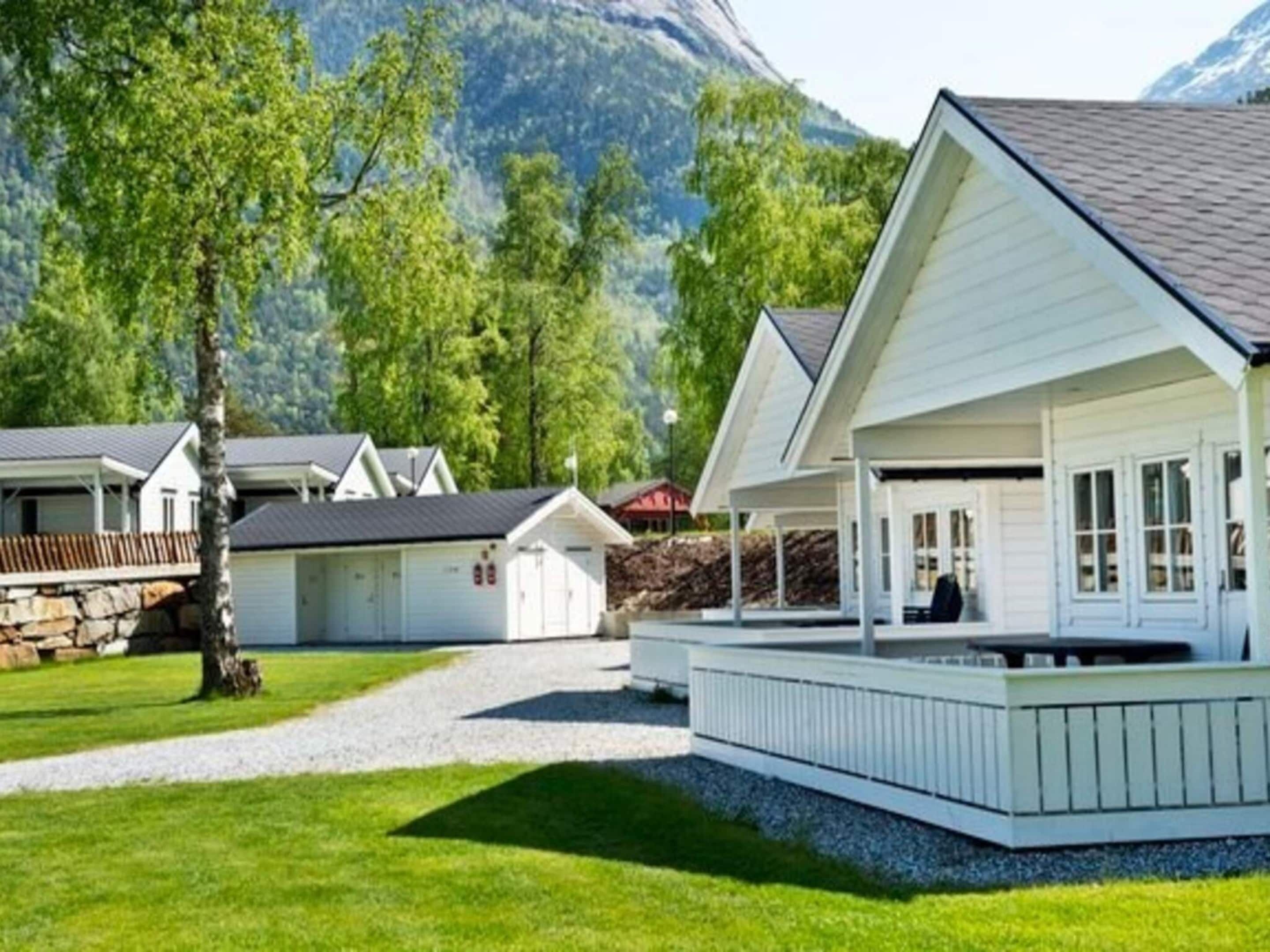 A white building with a covered porch and a stone wall in a mountainous area.