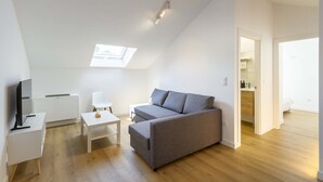 A modern living room with a grey sofa, a white side table, a flat-screen TV, and a skylight. - Urbanfive 5A Ourense center Duplex Penthouse with terrace (Ourense)