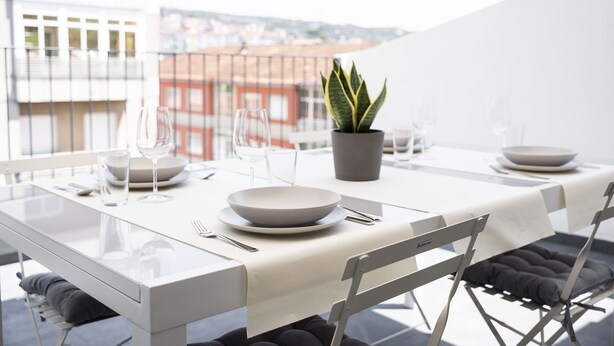 A modern dining area with a white table set for two, including plates, glasses, and cutlery. A potted plant is on the table, and the setting overlooks a cityscape. - Urbanfive 5A Ourense center Duplex Penthouse with terrace (Ourense)