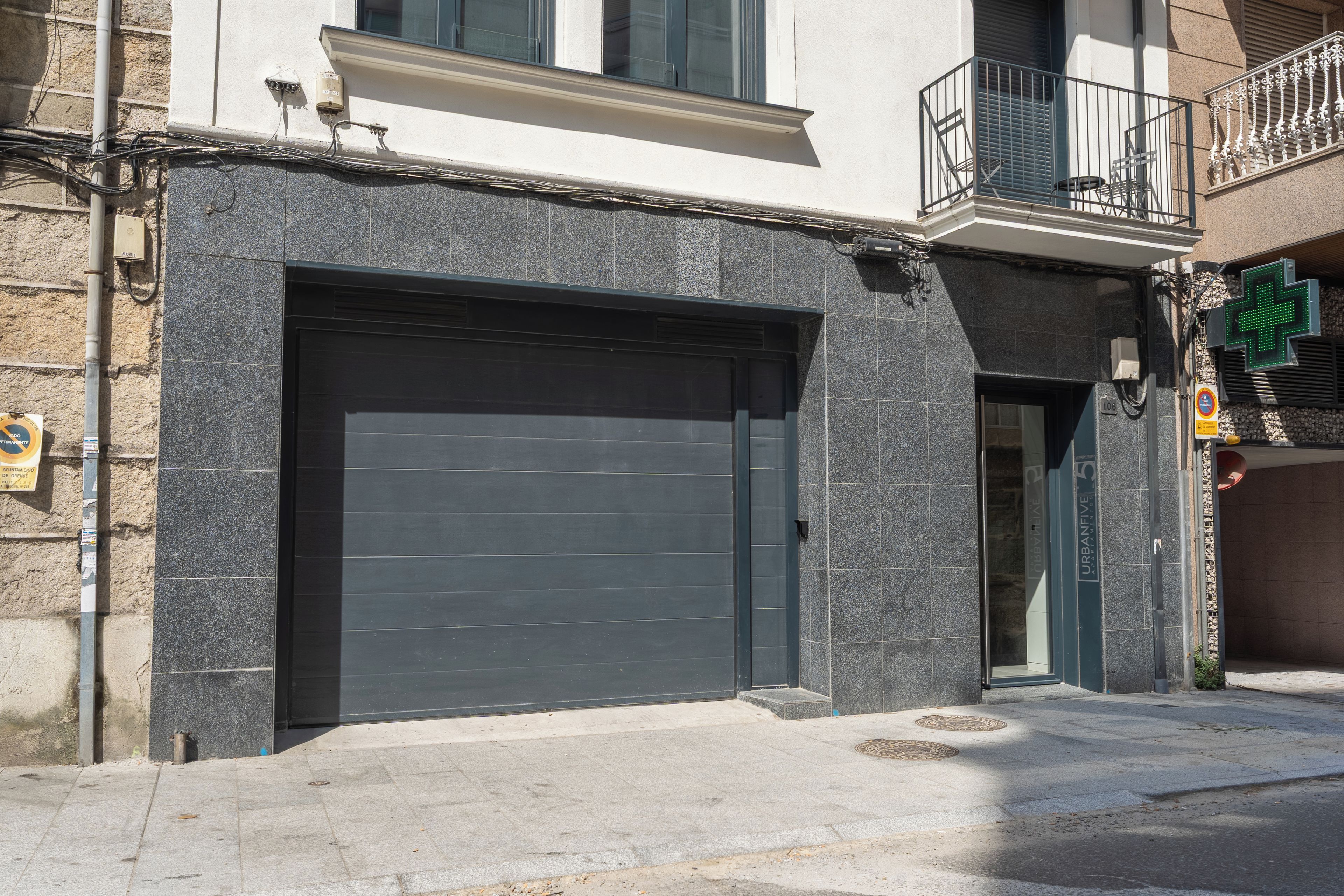 Un bâtiment doté d’un grand portail de garage, d’un balcon avec une rambarde en métal et d’un panneau indiquant la présence d’un établissement médical à proximité.