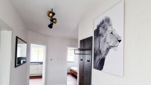 Un corridoio con pavimento in legno, una porta bianca, uno specchio e un quadro con l'immagine di una testa di leone.