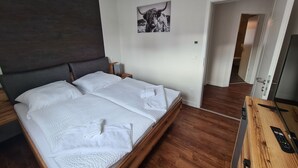 Una camera da letto moderna con un letto grande, una testiera in legno, un comodino con una lampada, un quadro appeso raffigurante un toro e una TV su un mobile in legno.