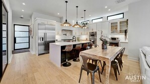 A modern kitchen with a central island, stainless steel appliances, pendant lighting, and a dining area with wooden chairs.